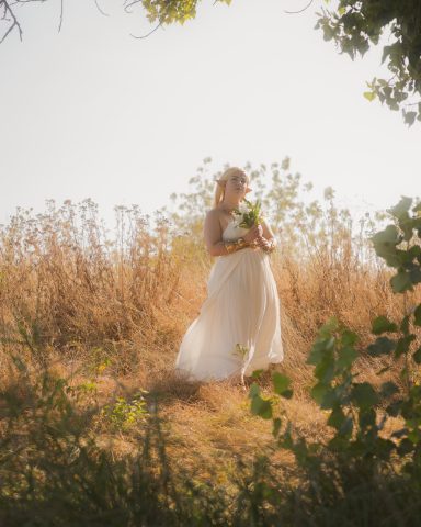Hochzeitsbraut in einem weißen Kleid, umgeben von goldenen Feldern und Pflanzen.