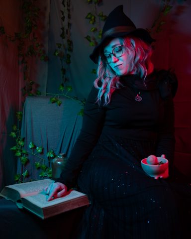 Frau in einem schwarzen Kleid und Hut, liest ein Buch in atmosphärischem Licht.