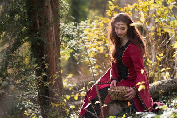 Eine Frau in einem roten Kleid sitzt im Wald und hält einen Korb in den Händen.